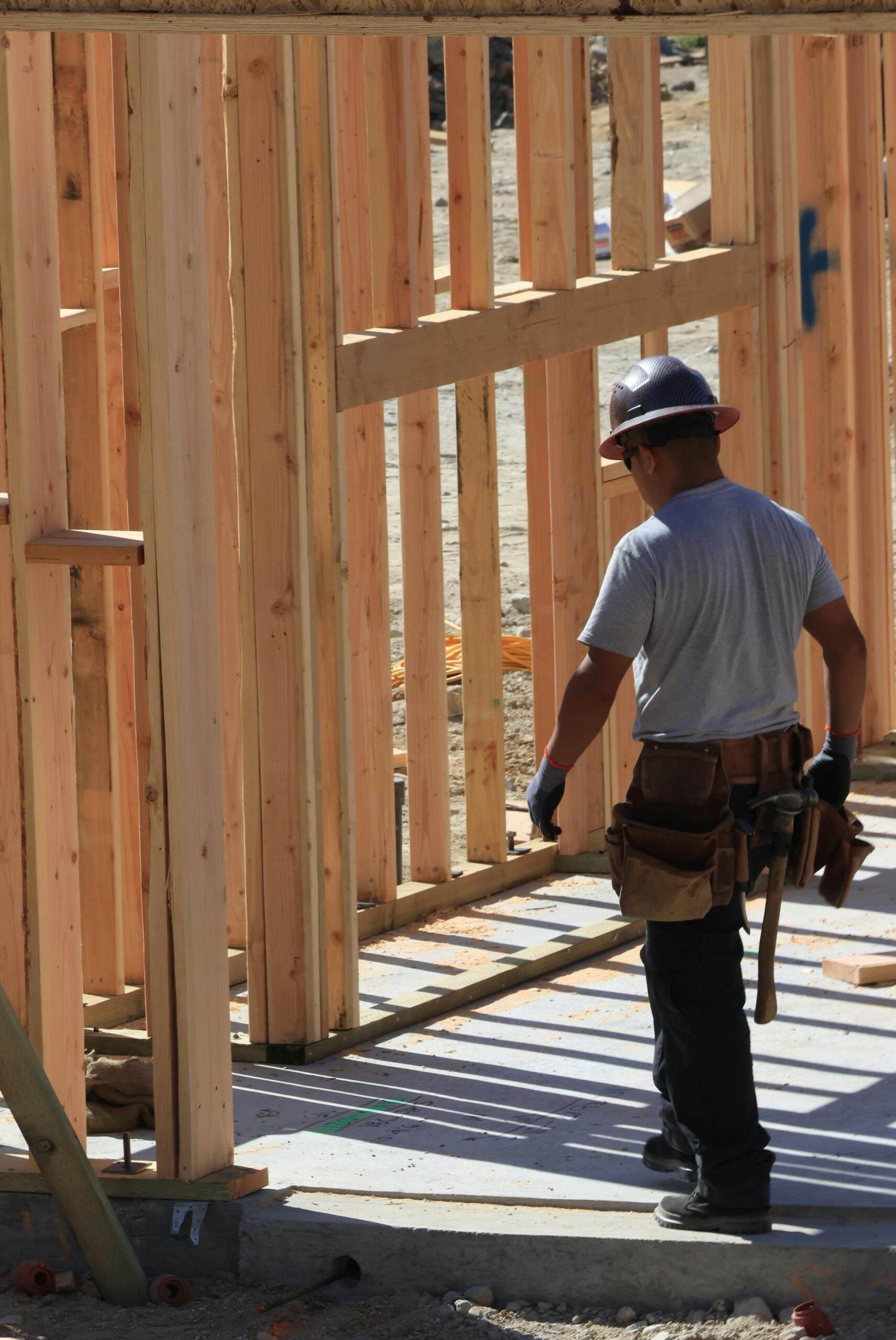This image depicts a construction worker at a job site. There is a wooden structure with beams. 