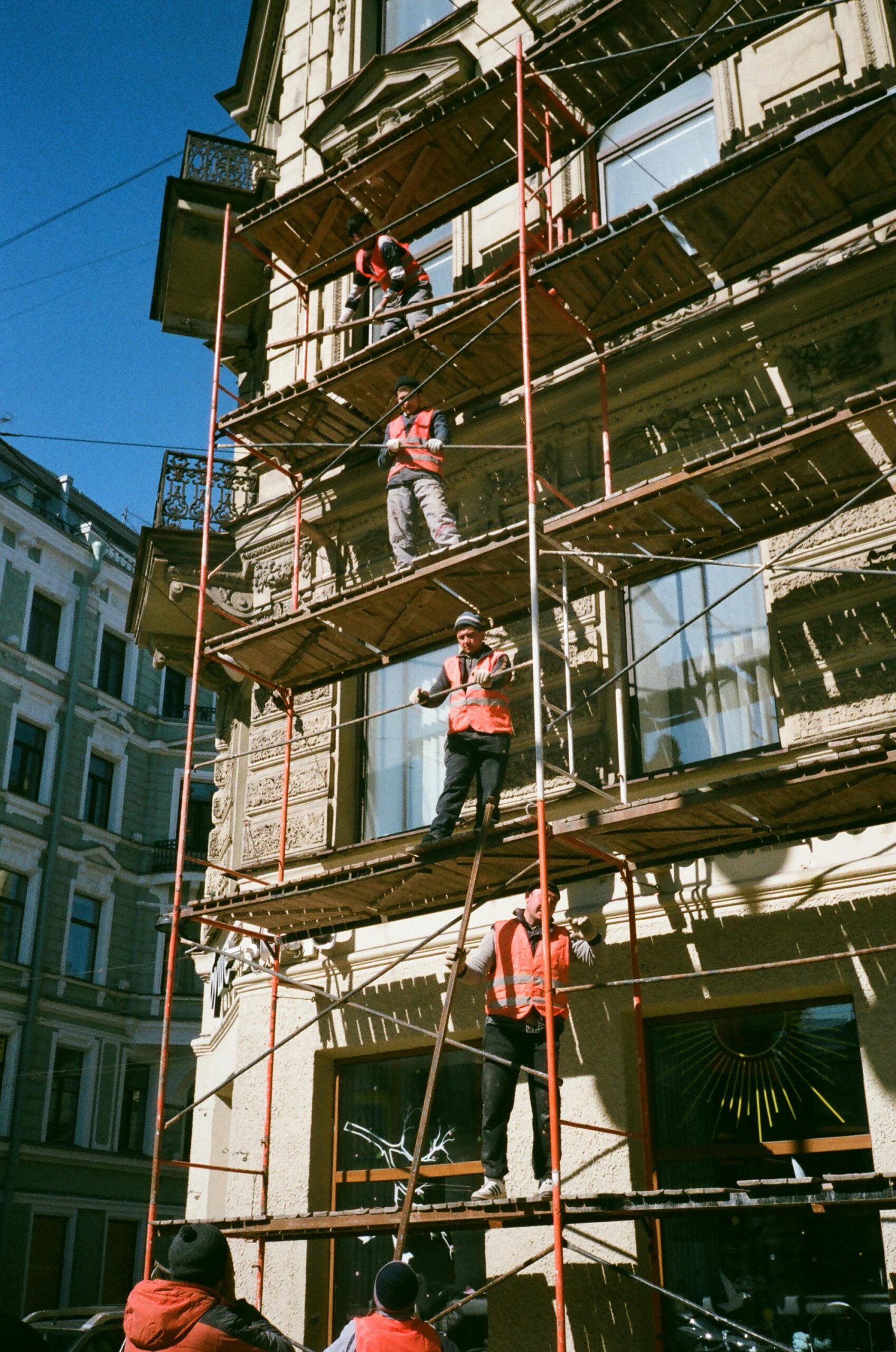  This image depicts construction workers working on five-story scaffolding against an urban building.