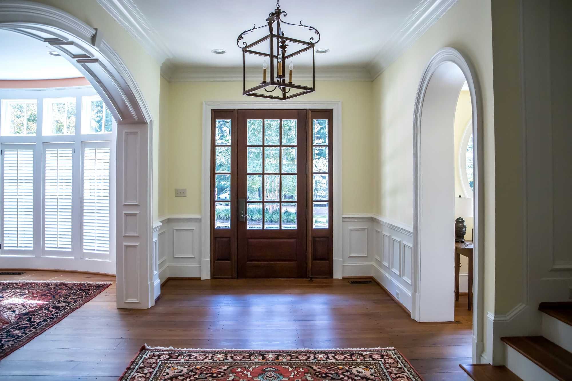 This image depicts a wide foyer in a home with large windows and a glass paneled door