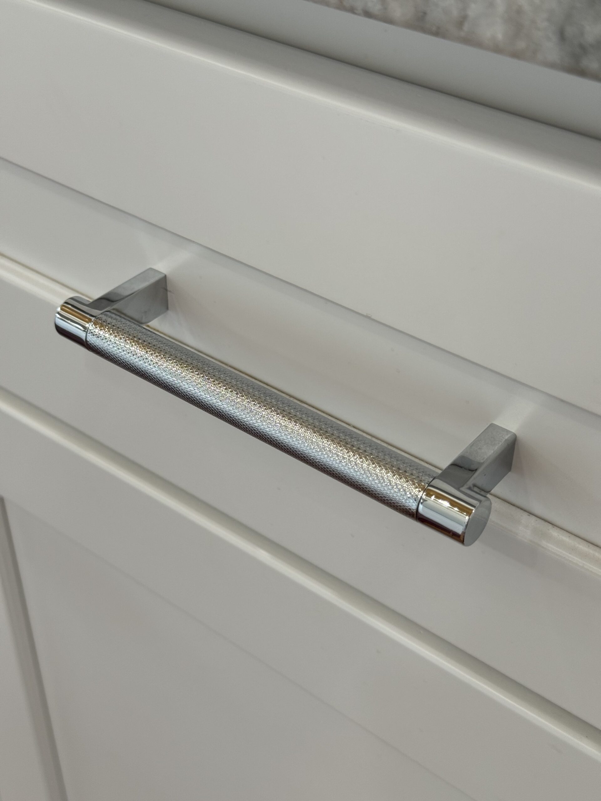 A close-up image showcases a stunning chrome cabinet pull against white cabinetry.