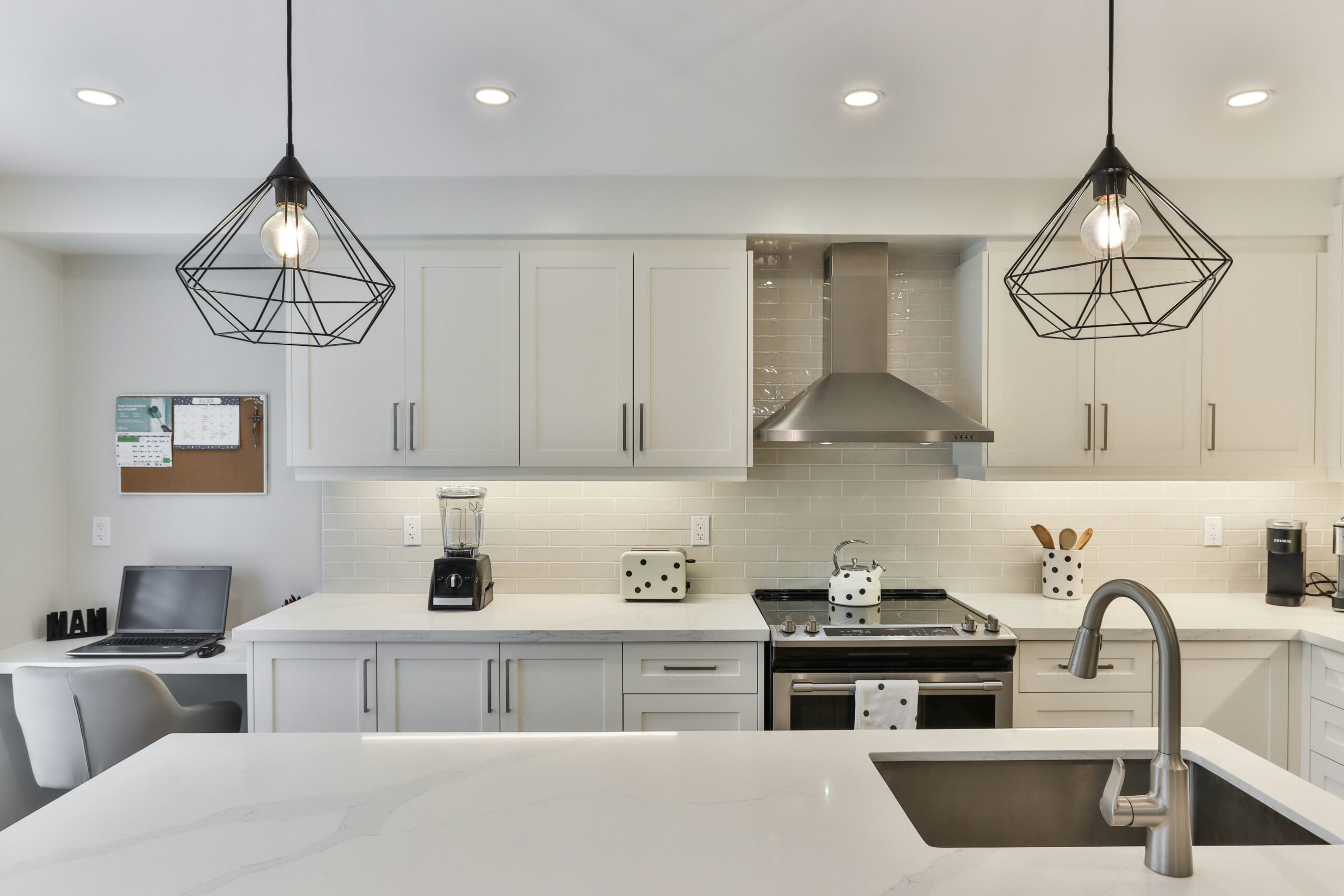 A clean, modern kitchen has white cabinets, a large kitchen island, quartz countertops, stainless steel appliances and black hardware.