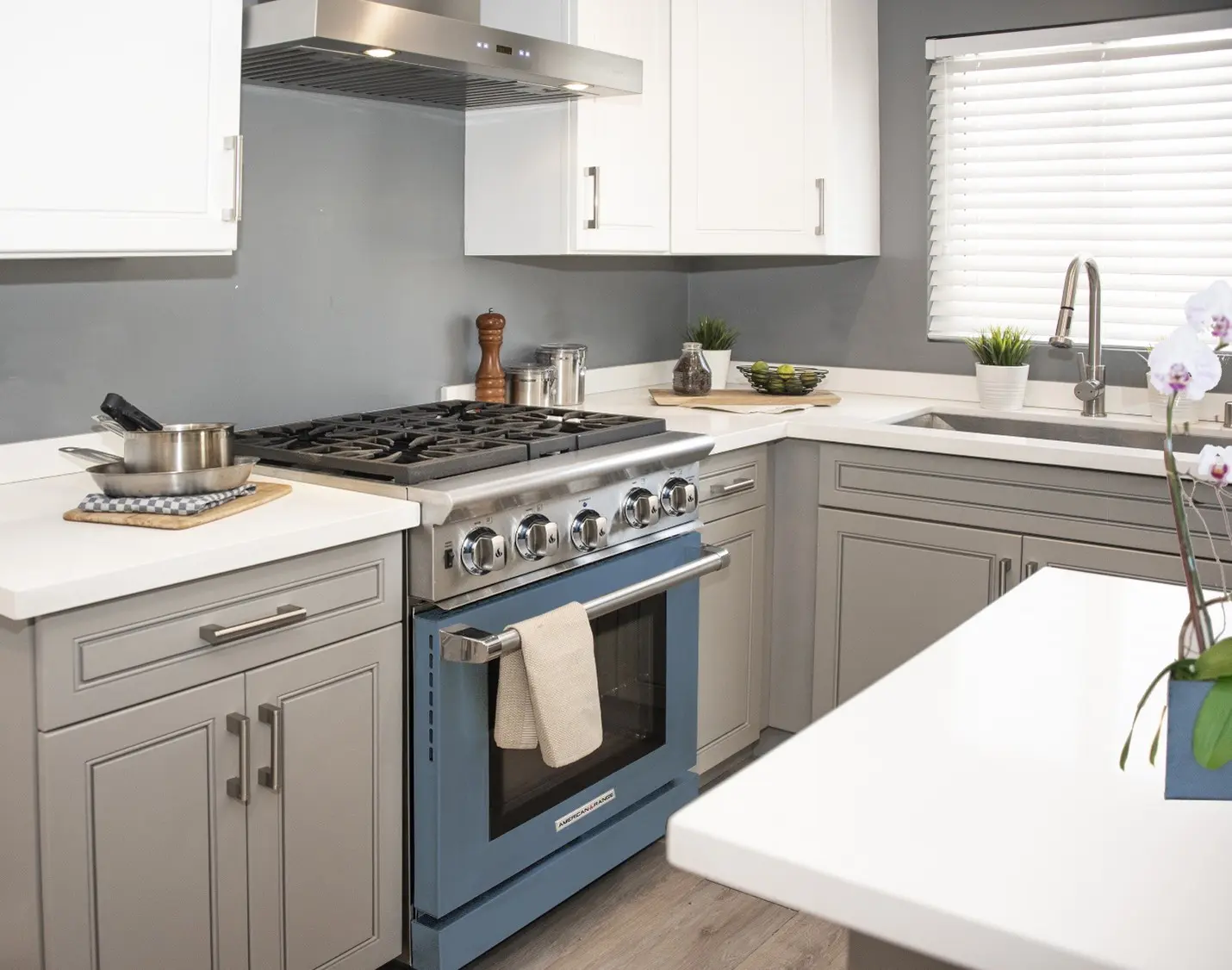 A modern kitchen has white countertops, grey cabinets and an eye-catching blue oven.