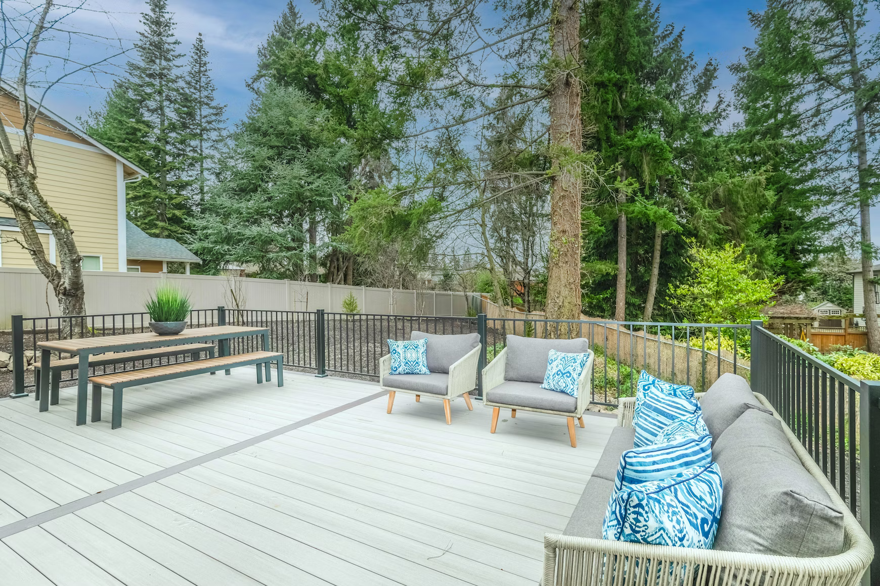 A large backyard deck features an eating area and a lounging space with two chairs and a sofa.