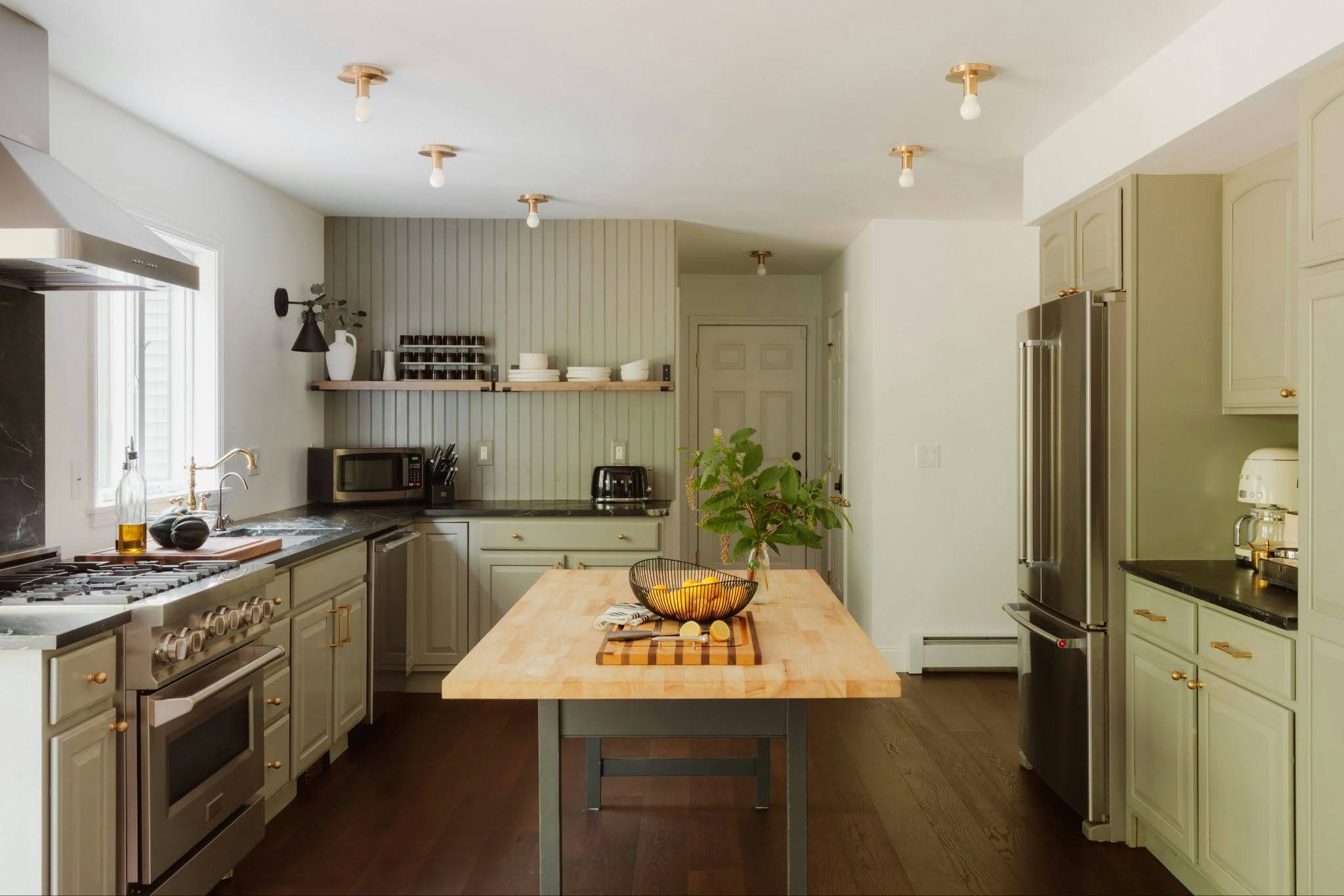 A modern kitchen has sage green cabinets and a butcher block island.