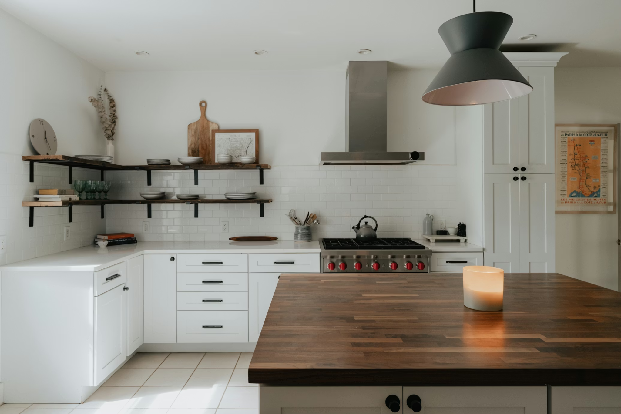 A kitchen has white cabinets and a large, dark butcher block island with a candle on it.