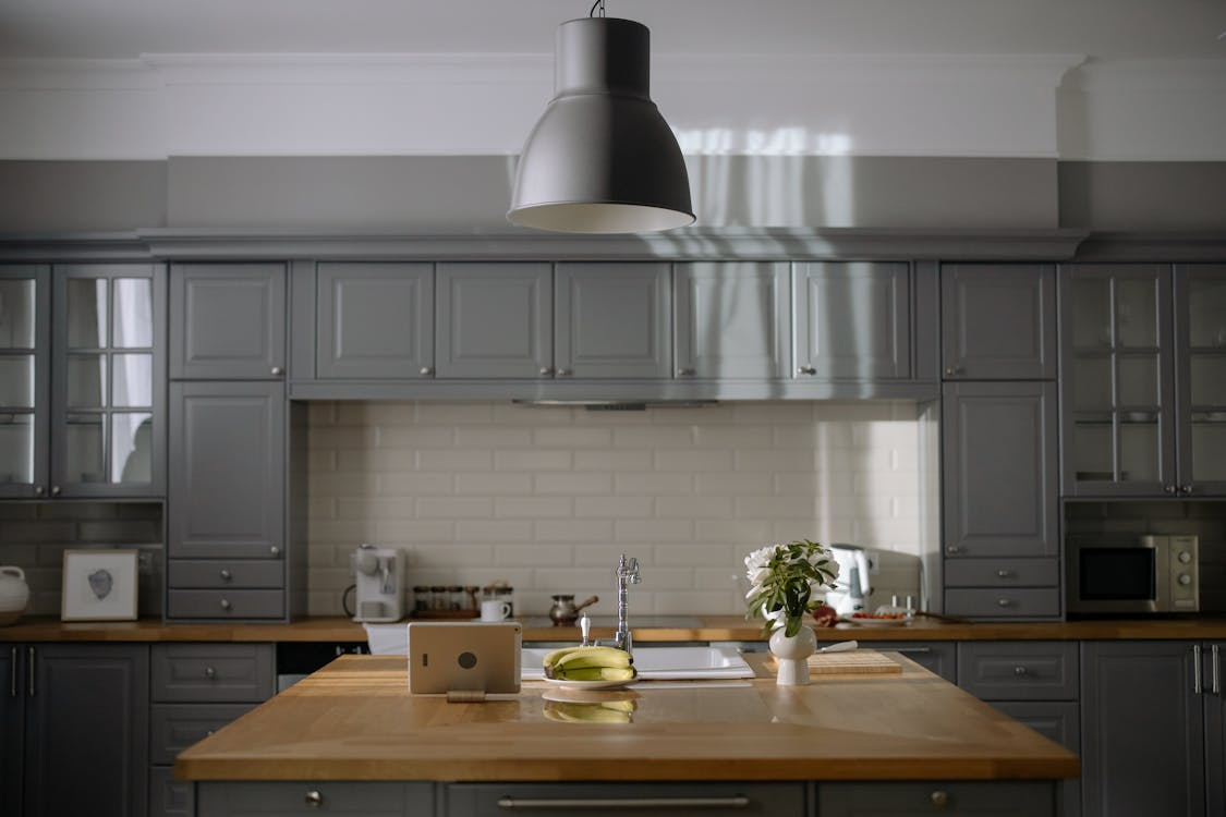 A modern kitchen with grey cabinets features a butcher block island with a sink.