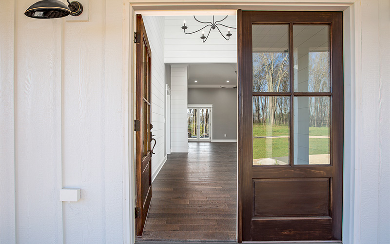Double wooden front doors with glass panels open into a bright, sunlit interior.