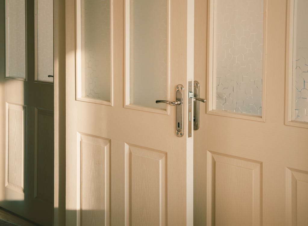 Double cream-colored front doors have frosted glass panels and silver hardware.