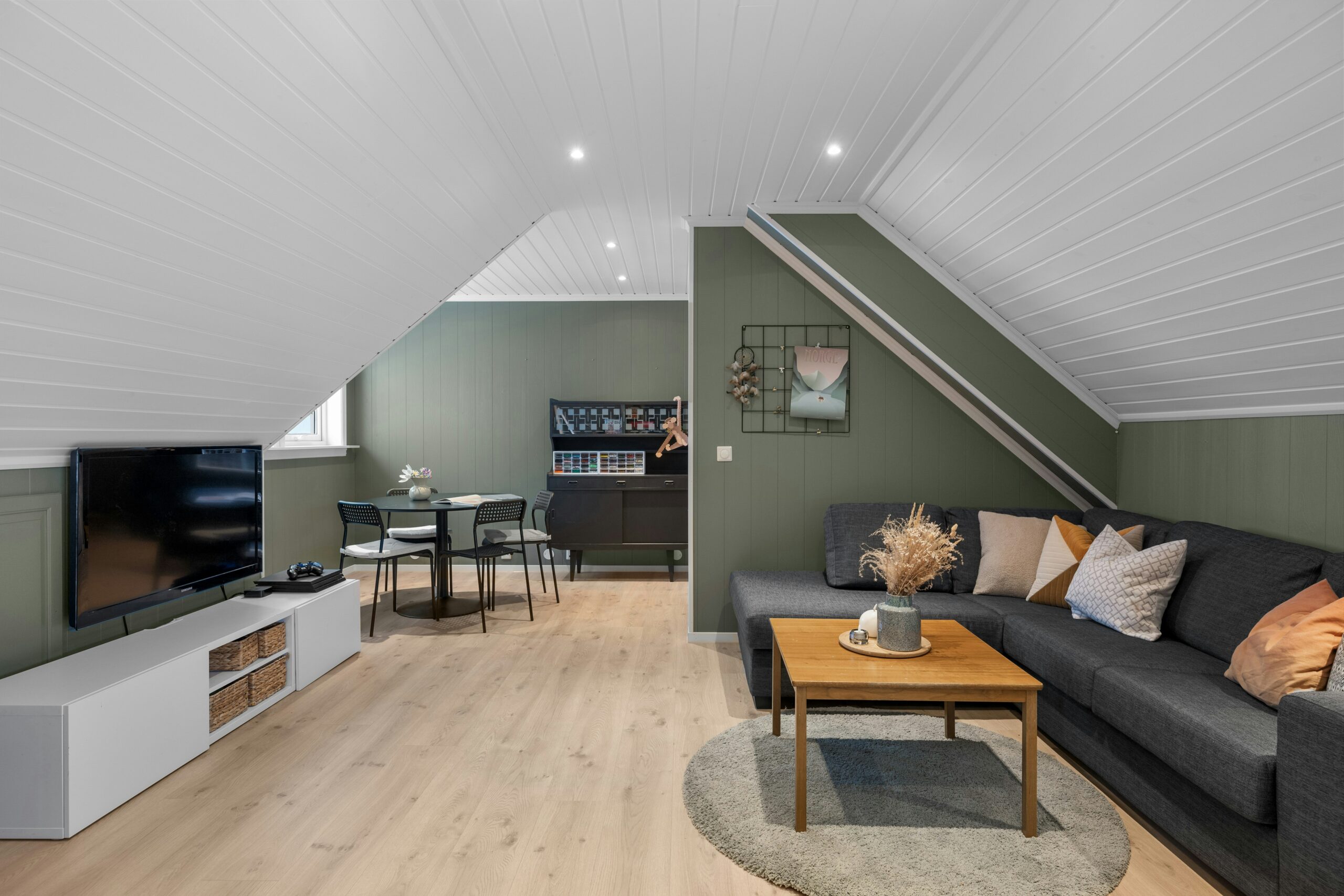 Cozy attic lounge area styled with a comfortable sofa, low coffee table and a mounted flat-screen TV in a converted roof space.