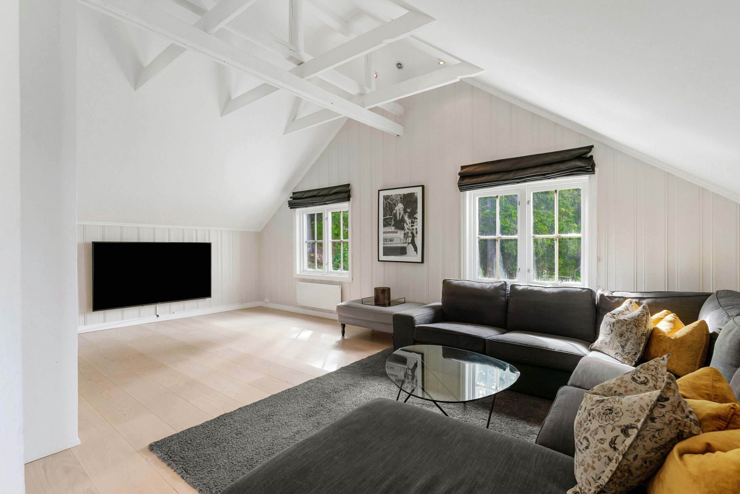 Living space built into an attic conversion with sloped ceilings, modern seating and a TV setup.