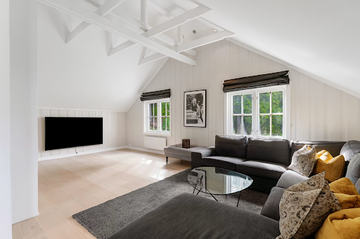 Living space built into an attic conversion with sloped ceilings, modern seating and a TV setup.