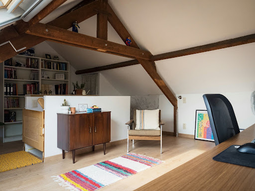 A modern attic-based home office with a built-in bookshelf, desk and colorful rugs.